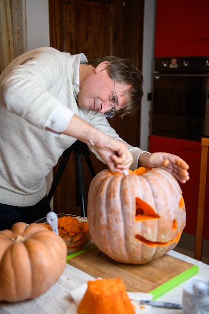 A middle age man father carving big orange pumpkin into jackolantern for Halloween holiday decoration at kitchen