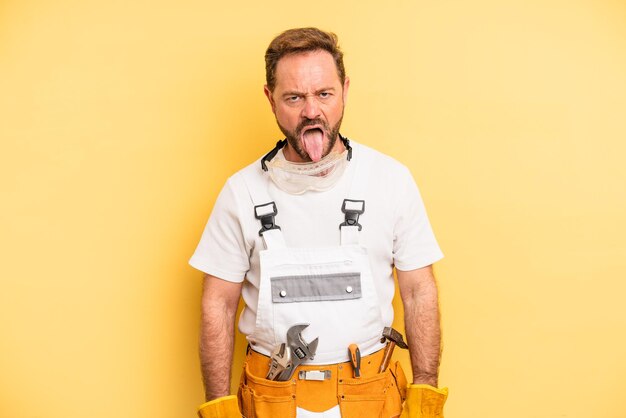 Photo middle age man feeling disgusted and irritated and tongue out. handyman and repair concept