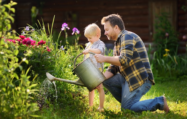 Middle age man and his little son watering flowers in the garden at summer sunny day