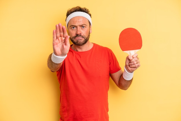 Photo middle age man looking serious showing open palm making stop gesture. ping pong concept