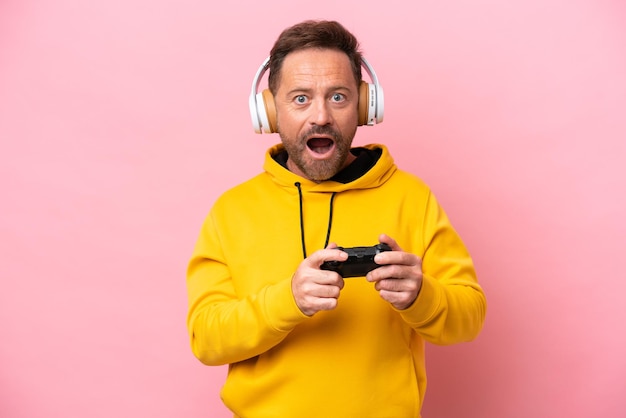 Middle age man playing with a video game controller isolated on pink background