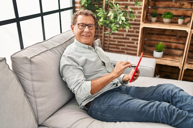 Middle age man using touchpad sitting on sofa at home