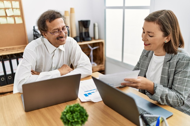 Middle age man and woman business workers using laptop and document working at office