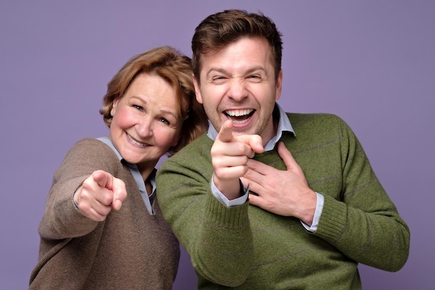 Middle age mother and son laughing on you pointing to the camera with finger