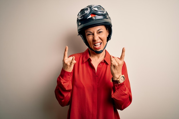 Middle age motorcyclist woman wearing motorcycle helmet over isolated white background shouting with crazy expression doing rock symbol with hands up Music star Heavy concept