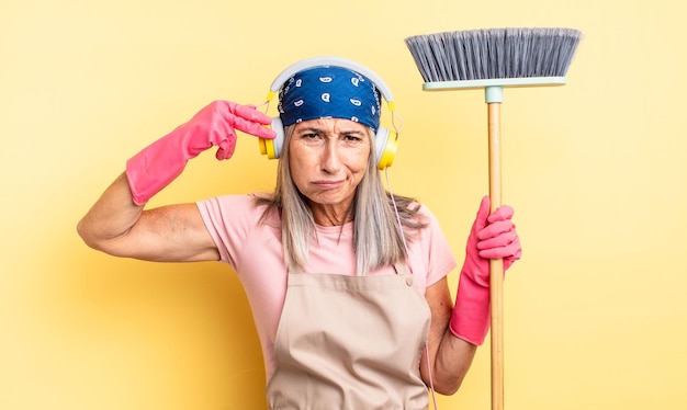 Middle age pretty woman looking unhappy and stressed, suicide gesture making gun sign. household and broom concept