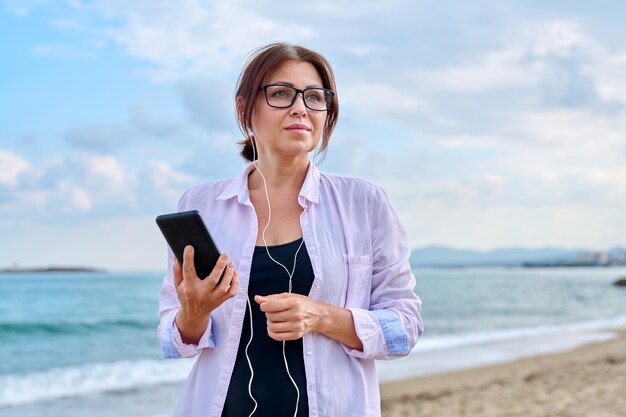 Middle age sad serious woman in headphones with smartphone outdoor