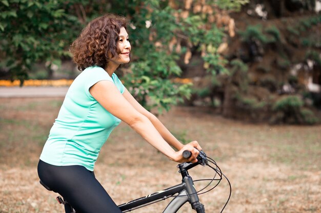 Middle age senior woman on bike cycle ride in countryside park outdoor.