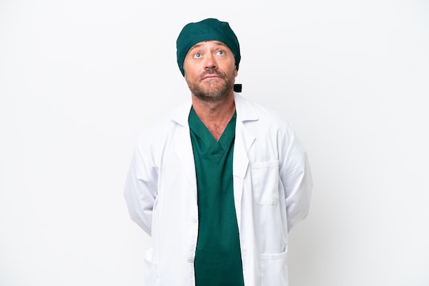 Middle age surgeon in green uniform isolated on white background and looking up