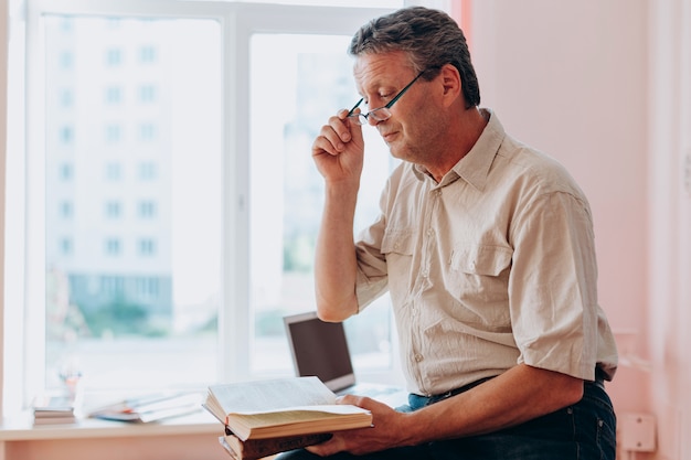 Middle age teacher in glasses sitting and reading a textbook.