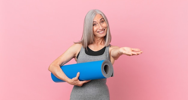 Middle age white hair woman smiling happily with friendly and  offering and showing a concept and holding a yoga mat. fitness concept