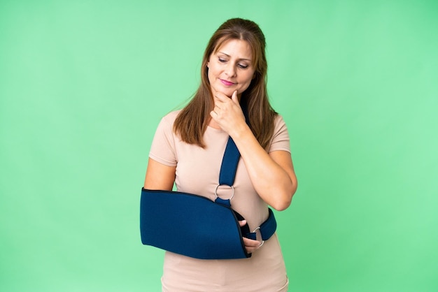 Middle age with broken arm and wearing a sling over isolated background looking to the side and smiling