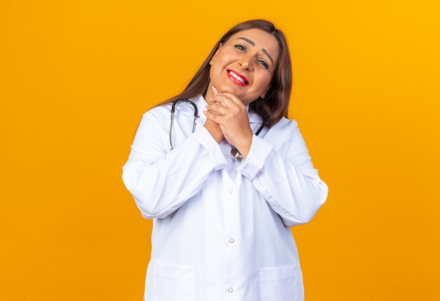 Middle age woman doctor in white coat with stethoscope happy and positive smiling cheerfully