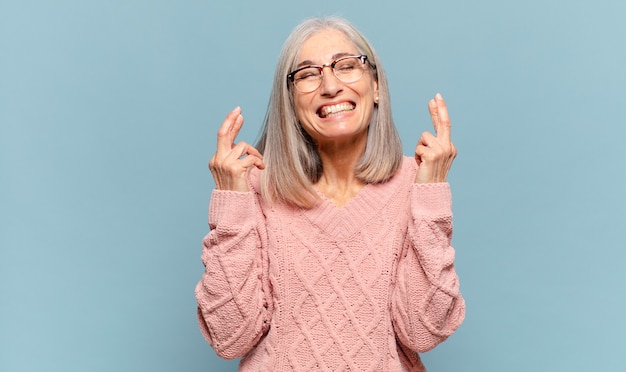 Middle age woman feeling nervous and hopeful, crossing fingers, praying and hoping for good luck