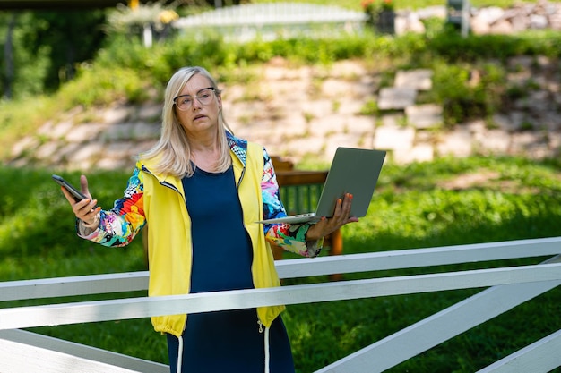 Middle age woman at the garden working from home using laptop and speaking on the phone