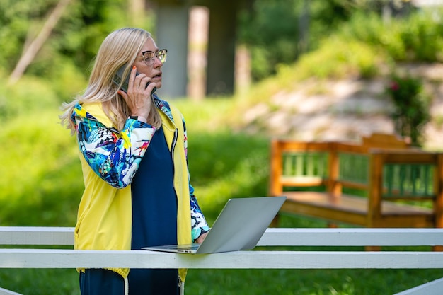 Middle age woman at the garden working from home using laptop and speaking on the phone