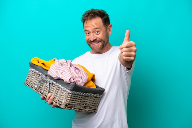 Middle age woman holding a clothes basket isolated on blue background with thumbs up because something good has happened