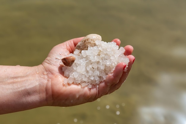 Photo middle age woman holding salt crystals in her hand from the dead sea