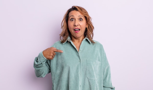 Middle age woman looking shocked and surprised with mouth wide open, pointing to self