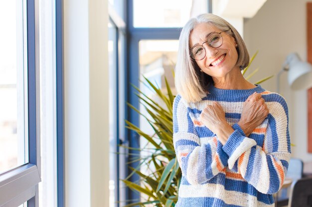 Middle age woman smiling cheerfully and celebrating, with fists clenched and arms crossed, feeling happy and positive