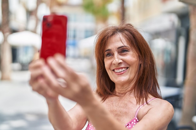 Middle age woman smiling confident making selfie by the smartphone at street