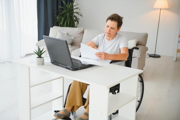 Middle age woman using laptop sitting on wheelchair at home