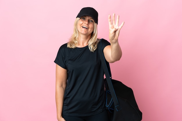 Middle age woman with sport bag isolated on pink happy and counting four with fingers