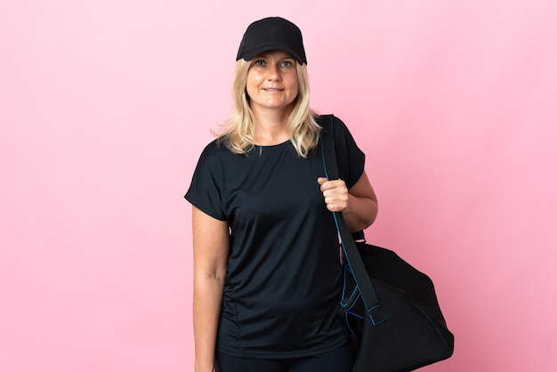 Middle age woman with sport bag isolated on pink wall looking side