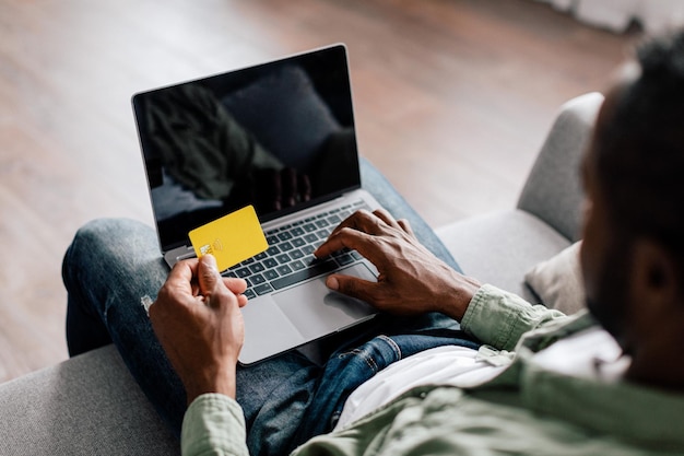 Middle aged african american guy typing on computer with blank screen and showing credit card