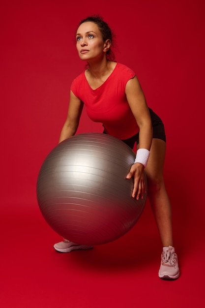 Middle aged African American sporty woman female athlete exercising with fitness ball against red background with copy ad space for advertising text