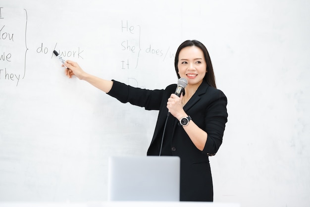 A middle-aged Asian woman teacher hold the microphone in classroom white board at University