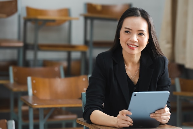 A middle-aged Asian woman teacher holding a tablet sitting in the classroom at University