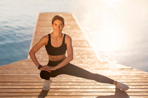 Middle Aged Athletic Woman Exercising On Wooden Pier Outdoors