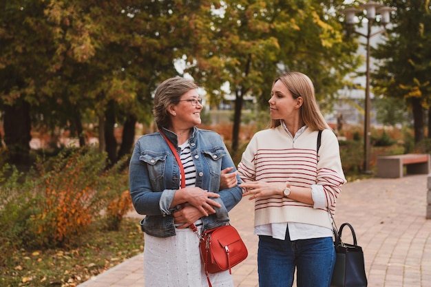 Middle aged blond mother and adult daughter walks and having fun in autumn park