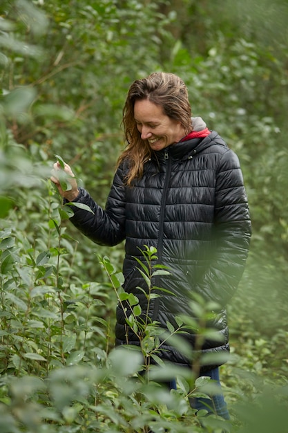 Middle-aged blond smiling woman walking in the bush in winter, among tree leaves. He wears a warm jacket.