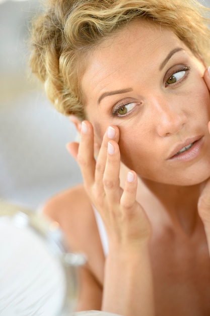 Middle-aged blond woman putting cosmetics on 