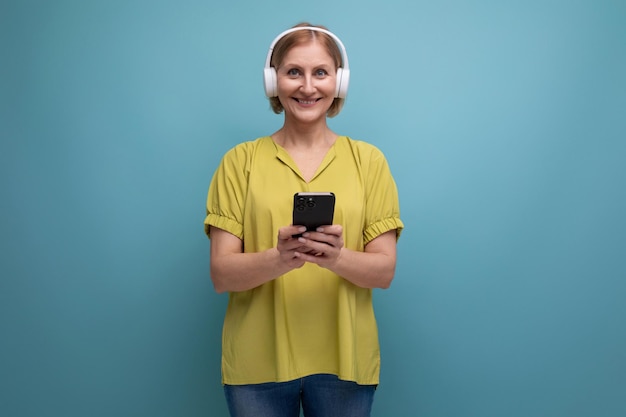 Middle aged business blond woman watching video on smartphone using headset for sound