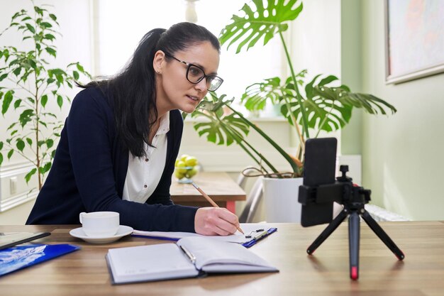 Middle aged business woman working from home remotely using smartphone for video call