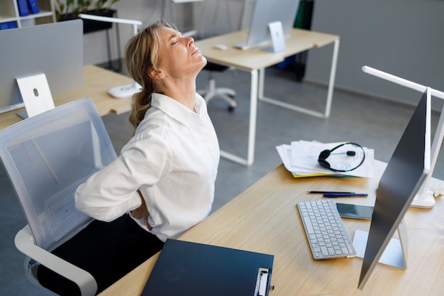 Middle aged businesswoman having back pain while sitting at office desk