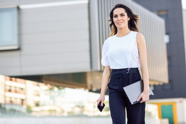 Middle-aged businesswoman working with her smart phone and laptop outdoors.