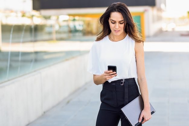 Middle-aged businesswoman working with her smart phone and laptop outdoors.