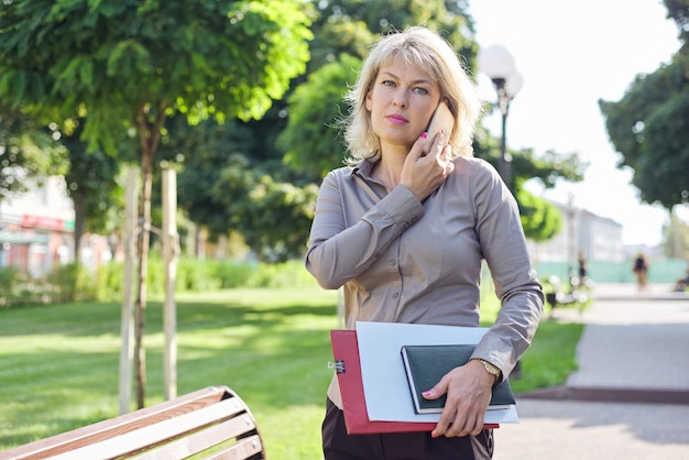 Middle-aged confident business woman talking on smartphone, portrait of successful female in city