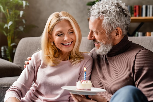 Middle aged couple holding cake celebrating wife's birthday at home