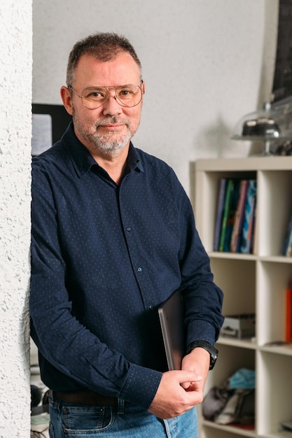 Middle-aged designer standing in his studio with a laptop under his arm