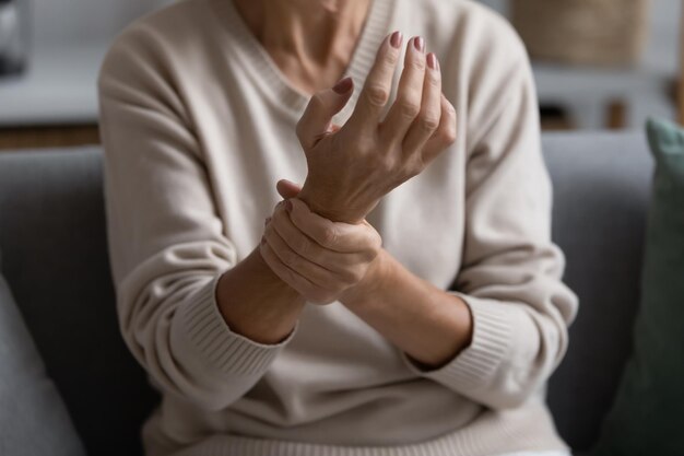 Photo middle aged elderly woman feeling wrist pain sitting on couch at home holding arm senior 60s pensioner suffering from rheumatoid arthritis joints ache muscle strain inflammation close up