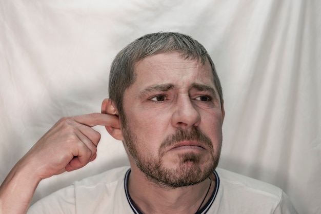 A middle-aged European man with a beard picks his ear with his finger.