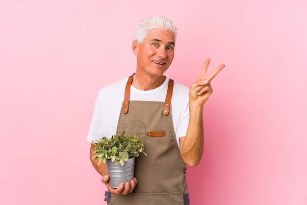 Middle aged gardener man isolated joyful and carefree showing a peace symbol with fingers.