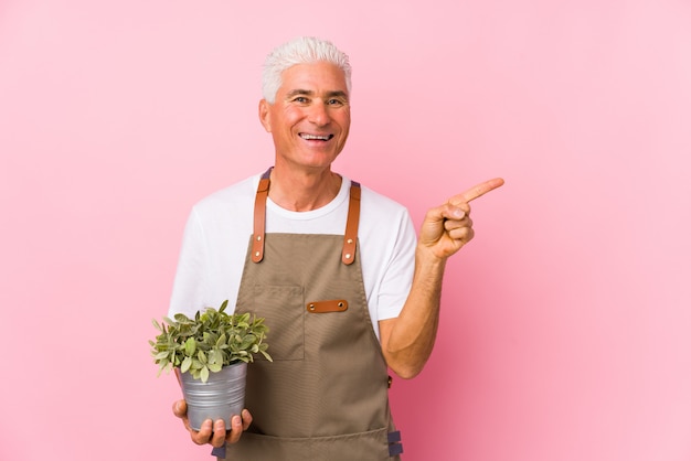 Middle aged gardener man isolated smiling and pointing aside, showing something at blank space.