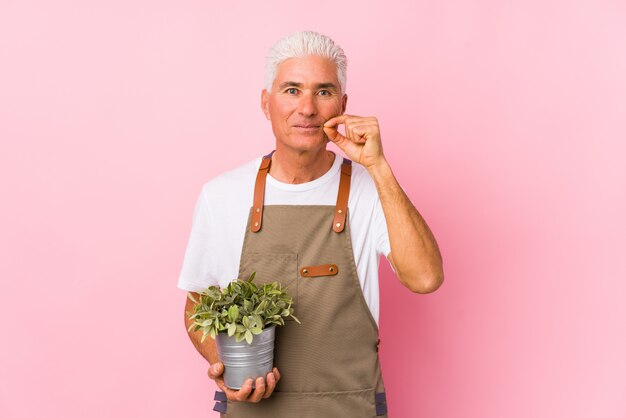 Middle aged gardener man isolated with fingers on lips keeping a secret.