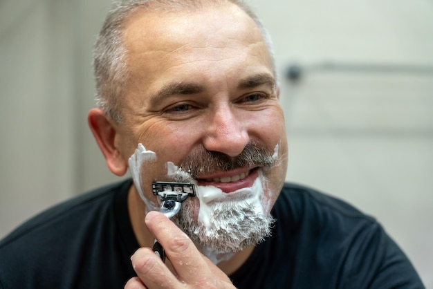 Middle aged handsome man shaving his beard in bathroom